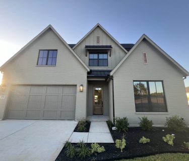 Front view of a modern, newly painted two-story house in Fort Worth with a neutral color scheme, featuring a double garage and landscaped front yard under a clear blue sky.